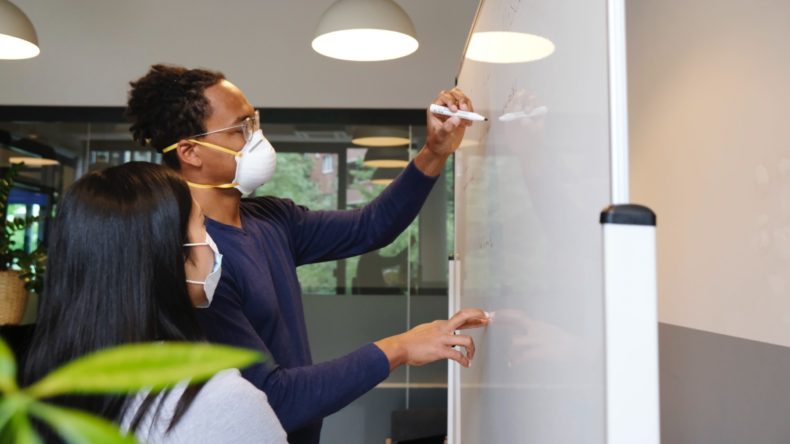 employees writing on whiteboard face masks