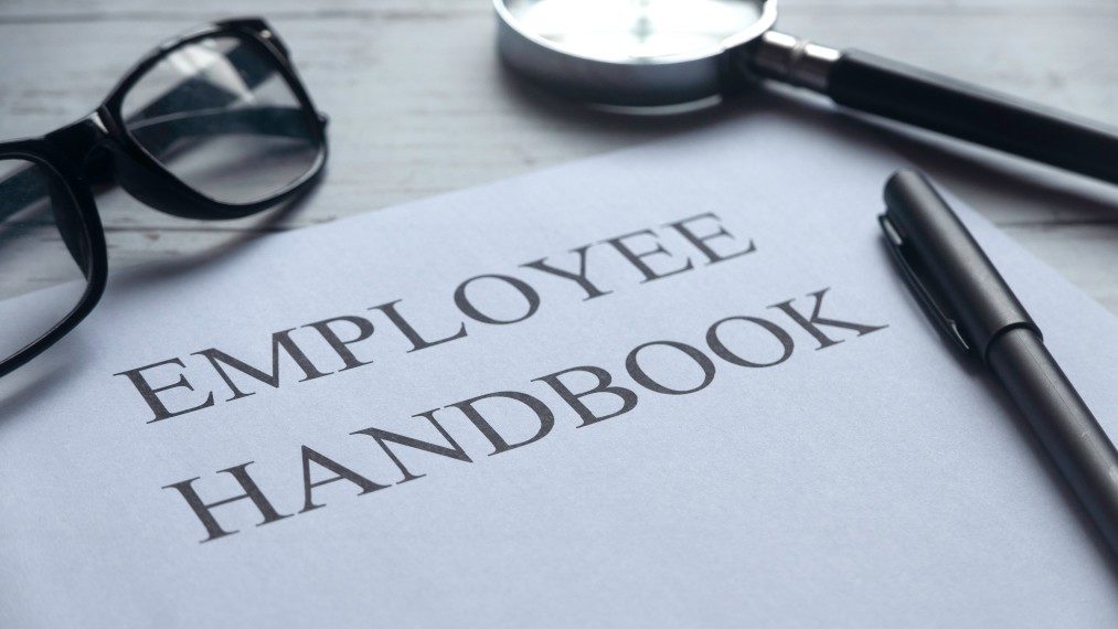 employee handbook with pen and magnifying glass