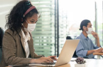 Asian young businesswoman working on computer in office with new normal lifestyle concept. Man and woman wear protective face mask and keep distancing to prevent covid virus after company reopen again
