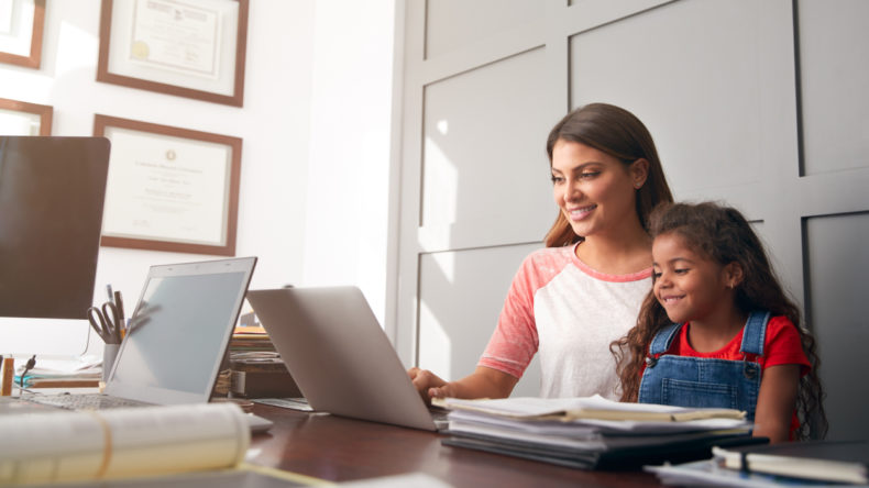 Hispanic Mother And Daughter Using Laptop In Home Office Together