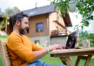 Side view of mature man with laptop working outdoors in garden, home office concept.