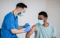 Doctor in face mask giving covid-19 vaccine injection to black male patient during vaccination campaign at clinic. Young African-American man getting immunized against infectious disease at hospital