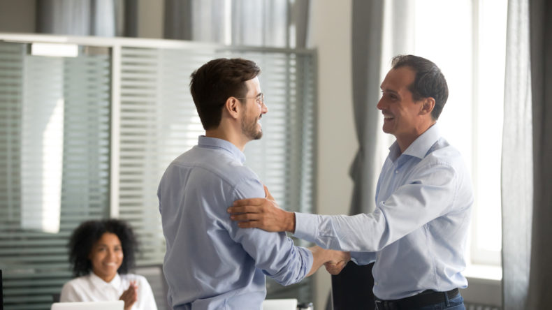 Smiling middle-aged ceo promoting motivating worker shaking hands congratulating with achievement promising respect bonus thanking for good work, team applauding, employee reward recognition concept