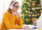 Happy pretty young woman freelancer in headphones smiling, working remote at laptop at home before Christmas