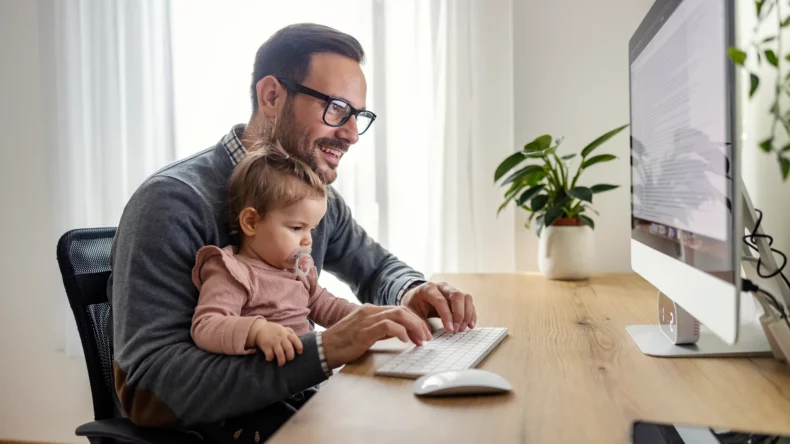 picture of father and baby enjoying the benefits of paternity leave together in front of a computer