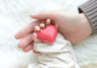 picture of baby's hand holding heart and parent handing holding baby hand
